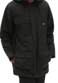 Giacca nera isolata con cappuccio, dotata di due tasche sul petto e due tasche inferiori, realizzata in tessuto resistente con chiusure a bottone.