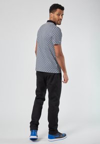 Lyhythihainen polo sinisenä, geometrisella kuviolla ja mustalla kauluksella, yhdistettynä mustiin housuihin ja sinisiin urheilukenkihin. Pehmeä kangaskuvio.