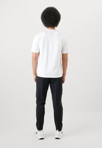 Fehér, rövid ujjú ing, a hátsó felső részén hálós betéttel, fekete nadrággal és fehér sportcipővel párosítva, hátulról nézve.