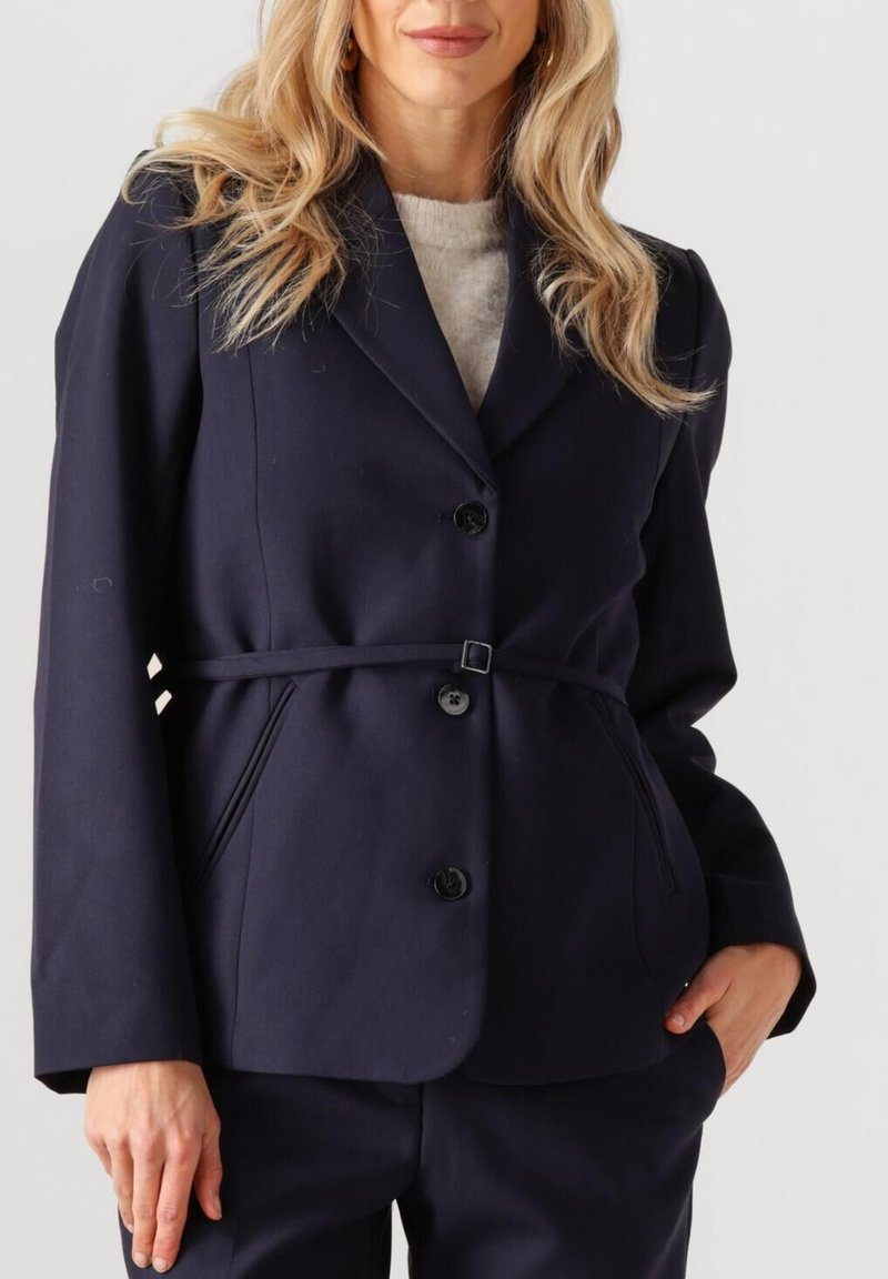 Marineblauwe blazer met een getailleerde pasvorm, sluiting met één knoop en een tailleband. Voorzien van revers en twee zijzakken. Glad stoftextuur.