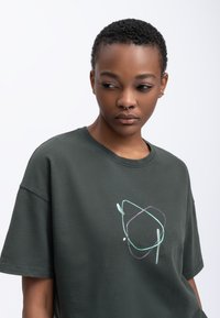 Donkergroen oversized t-shirt van katoen; beschikt over een abstract lichte blauwe en paarse print op de borst; relaxte pasvorm, korte mouwen.