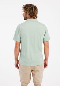 Lichtgroen polo shirt met korte mouwen en een kraag, gemaakt van zachte stof; gedragen met beige shorts, gezien van achteren.