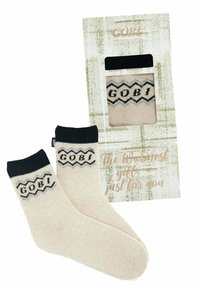 Beige kashmirstrumpor med en svart manschett och zigzag-mönster; förpackade i en texturerad presentlåda med fönster.