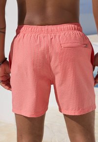 Rosa gestreifte Schwimmshorts mit einem elastischen Bund, ausgestattet mit Seitentaschen und einer Reißverschlusstasche auf der Rückseite. Texturiertem Stoff mit lockerem Sitz.
