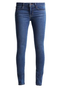 Jeans ajustados en denim azul oscuro. Presentan un diseño clásico de cinco bolsillos, pasadores para cinturón y un cierre de cremallera con botón. Textura suave.