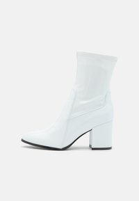 Bílé lakované kožené ankle boty s blokovým podpatkem, které se vyznačují elegantním, těsným designem a lesklým povrchem.