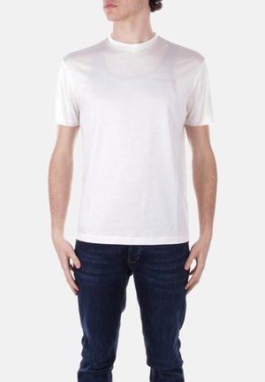 T-shirt bianco a maniche corte realizzato in un materiale liscio, caratterizzato da un colletto a girocollo e un sottile logo sul petto. Abbinato a jeans scuri.