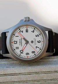 Timex Expedition Uhr mit weißem Zifferblatt, schwarzen und roten Zeigern, schwarzem Lederarmband, Datumsanzeige auf 3 Uhr und titanhaltigem, stoßfestem Gehäuse.