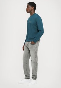 Teal sweatshirt med rund halsringning, med tryckt text; kombinerad med ljusgrå jeans och vita sneakers; mjukt tyg, avslappnad passform.