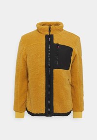 Giacca in pile gialla con colletto alto, tasca a pannello nera, chiusura con zip e accenti neri a contrasto sul davanti e sui polsini.