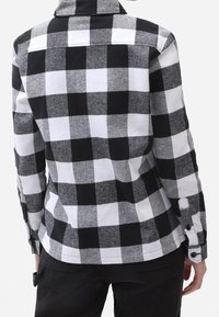 Czarna i biała koszula flanelowa w kratkę, z kołnierzykiem, guzikami na mankietach oraz miękkim, teksturowanym materiałem. Widoczne akcenty przeszyć.