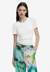 Vit t-shirt med kort ärm och rund halsringning, parat med ljusblå byxor med färgglada blommönster och resårmidja.