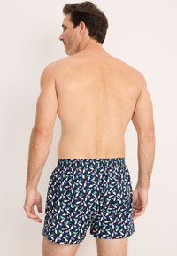 Blå mönstrade badshorts i lätt tyg, med en blandning av gröna och vita mönster. Elastisk midja för komfort.