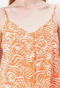 Top orange din material ușor, decorat cu un model de dungi albe de zebra, cu bretele subțiri și închidere cu nasturi în față.