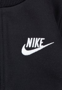 Fekete szövet texturált felülettel, fehér hímzett Nike logóval és pipa jellel, amelyek jól láthatóan a bal mellrészen helyezkednek el.