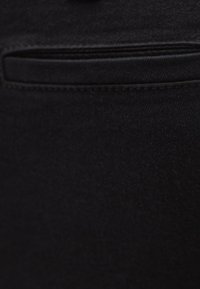 Czarna tkanina o gładkiej fakturze, z małą poziomą kieszonką i przeszyciami wzdłuż krawędzi.