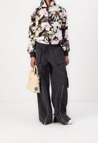 Bluza polarowa z kwiatowym wzorem w pastelowych kolorach, zestawiona z ciemnymi spodniami bojówkami z przednimi kieszeniami i zamkami błyskawicznymi. Jasna torba na ramię.