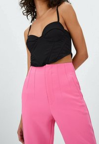 Haut court noir avec bonnets structurés, fines bretelles ; assorti à un pantalon rose taille haute à jambes larges, présentant des plis sur le devant et des poches.