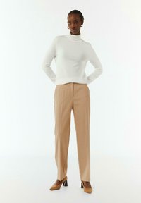 Maglione bianco a maniche lunghe con collo alto abbinato a pantaloni beige su misura e décolleté con punta. Tessuto liscio con una silhouette aderente.