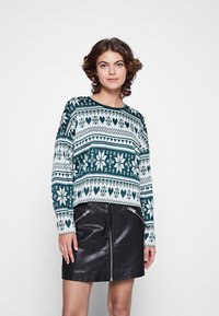 Žalias ir off-white raštuotas megztinis su ilgomis rankovėmis, puošti širdelių ir snaigių raštais, derinamas su juoda odine užtrauktuku sijonu.