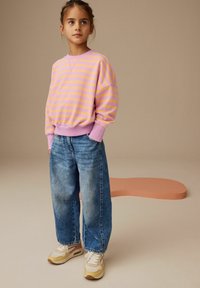 Rosa och gula randiga tröjor med lös passform, kombinerat med vida blå jeans och beige sneakers. Släta texturer och avslappnad stil.