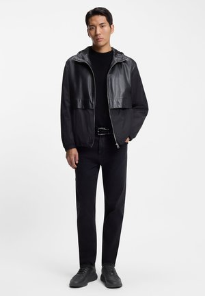 Black zip-up jacket in a mix of smooth synthetic and textured fabric. Paired with black jeans and sneakers, featuring a hood and elastic cuffs.