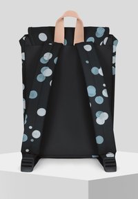 Svart ryggsäck med ett bubbelmönster i blått och vitt. Har ljusrosa remmar och en slät, matt yta, med justerbara svarta spännen.