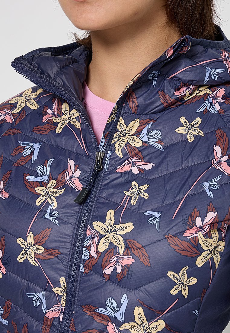 Chaqueta acolchada de color marino con patrón floral en rosa, amarillo y azul. Presenta un cierre con cremallera y textura acolchada. Llevada sobre una blusa rosa clara.