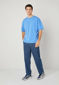 Modra prevelika majica s kratkimi rokavi, sproščenega kroja. Nosena z temno modrim naravnim krojem in sivimi športnimi čevlji z modrimi poudarki.