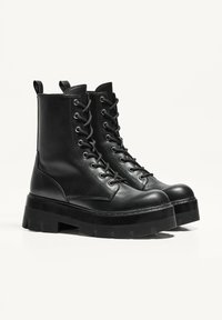 Botine negre din piele cu șireturi în față, vârf rotund, talpă groasă și bucle în spate pentru a fi ușor de încălțat.