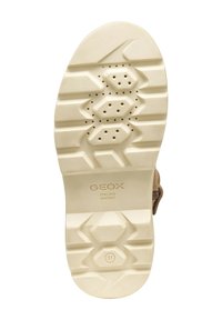 Semelle en caoutchouc crème avec un motif hexagonal et des trous de ventilation, arborant un branding textuel discret. Le design est épuré et fonctionnel.