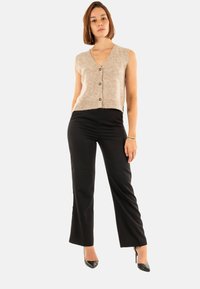 Gilet sans manches beige avec un décolleté en V profond et trois boutons, associé à un pantalon évasé noir et des chaussures à talons hauts noires.