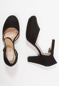 Czarne zamszowe szpilki z odkrytymi palcami i designem na odkrytej pięcie. Posiadają blokowy obcas i gładką podszewkę.