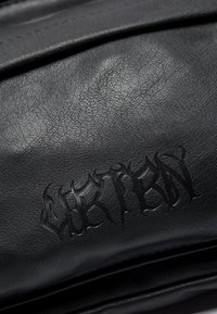 Black leather product featuring a textured surface, with raised flame-like accents and intricate lettering embossed into the material.
