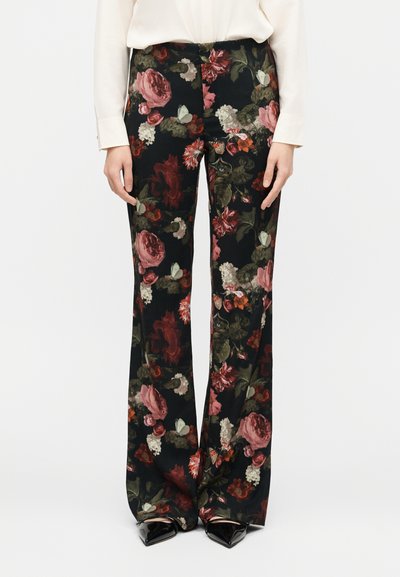 Woman wearing black wide-leg trousers with large pink and red floral pattern paired with a cream blouse and black pointed shoes.