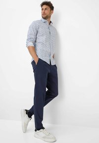 Camicia azzurra chiara con un motivo floreale, abbinata a pantaloni blu navy e sneakers bianche, caratterizzata da una vestibilità rilassata e maniche arrotolate.