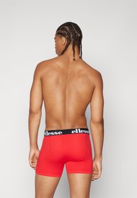 Rote Boxershorts mit einem schwarzen elastischen Bund, der das 'ellesse'-Logo trägt. Der Stoff wirkt glatt und anschmiegsam und ist für Komfort geeignet.
