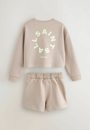 Kort, beige sweatshirt met grote ronde tekstafbeelding, gecombineerd met bijpassende shorts met elastische tailleband en zachte stofstructuur.