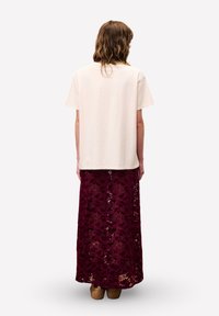 T-shirt crème à manches courtes associé à une longue jupe en dentelle bordeaux avec des motifs floraux et une finition texturée.