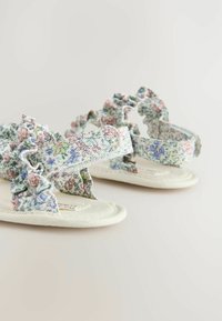 Sandały w kwiatowy wzór z falbaniastymi paskami z tkaniny w pastelowych kolorach. Materiał bawełniany z miękką, teksturowaną podeszwą i zaokrąglonymi krawędziami.