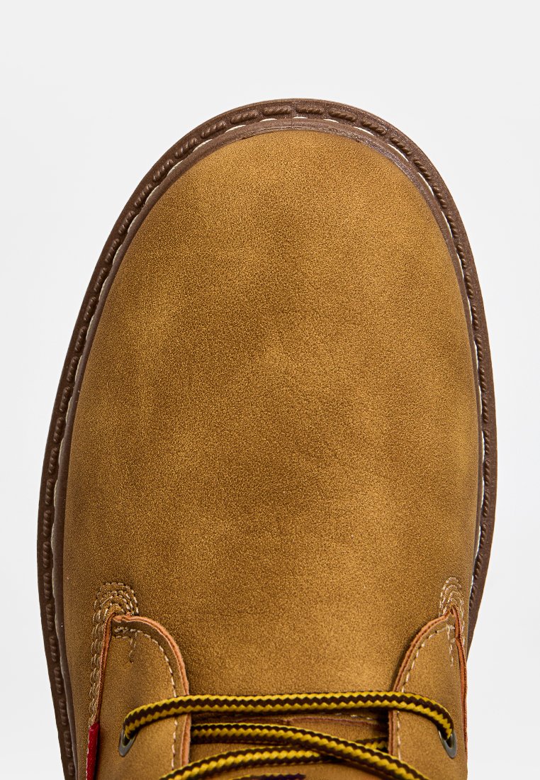 Brązowe zamszowe botki za kostkę z okrągłym noskiem, kontrastującymi żółtymi sznurowadłami i brązową gumową podeszwą. Posiadają detale w postaci przeszyć na krawędziach.