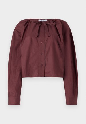 Bordo skraćena bluzica od laganog materijala, s vezicom na vratu, dugim rukavima i prednjim kopčanjem na dugmad. Glatka tekstura sa minimalnim detaljima.