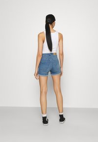 Shorts in denim con lavaggio chiaro, vita alta, orlo arrotolato e tasche posteriori classiche. Abbinati a una canottiera bianca e a scarpe da ginnastica nere.