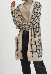Stickad lång cardigan i beige med svart rutmönster, med öppen front, långa ärmar och två framfickor. Mjuk textur.