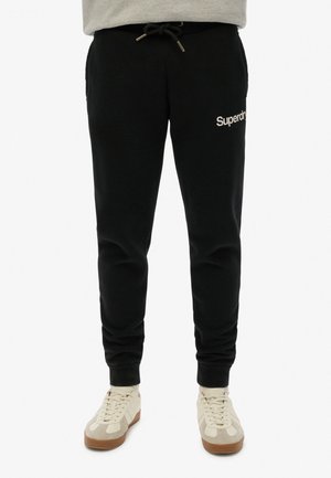 Sorte sweatpants med snoretræk i taljen, sidelommer og en hvid "Superdry"-logo på venstre lår, med en blød stoftekstur.