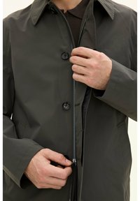 Mörkgrön vattentät jacka med ståkrage, knappstängning och blixtlås. Har en slät yta och en skräddarsydd passform.