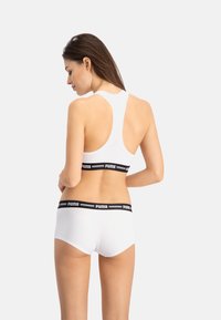 Sujetador deportivo blanco con diseño de espalda nadadora y banda con el logo negro de Puma, combinado con boxer blancos que presentan una banda en la cintura con un logo negro similar.