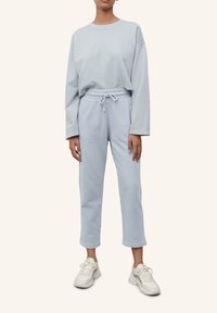 Svetle modrý teplákový komplekt z jemné látky; dlouhý rukáv, top s kleslými rameny, kalhoty s elastickým pasem a bílé tenisky. Jednoduchý design, volný střih.