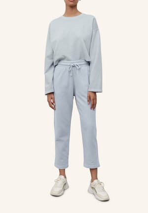 Lichtblauw trainingspak van zachte stof; lange mouwen top met verlaagde schouders, broek met drawstring taille, en witte sneakers. Eenvoudig ontwerp, relaxte pasvorm.