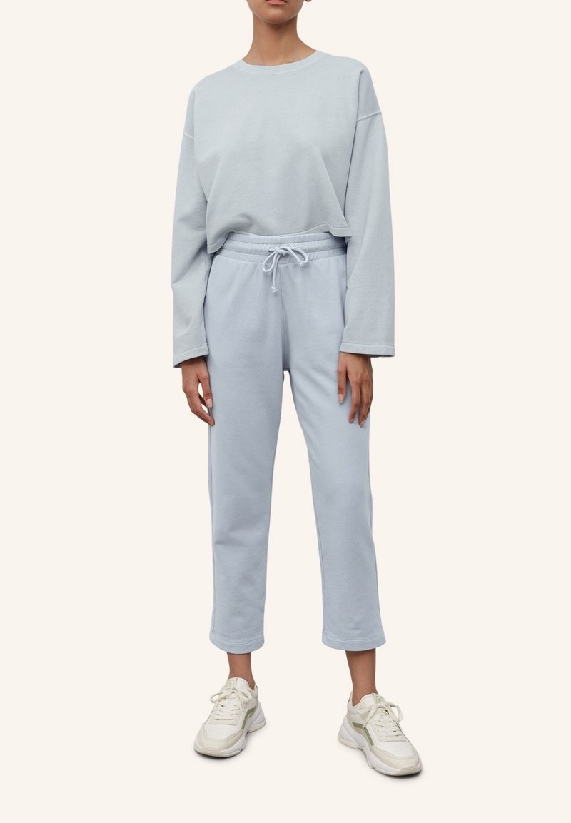 Svetle modrý teplákový komplekt z jemné látky; dlouhý rukáv, top s kleslými rameny, kalhoty s elastickým pasem a bílé tenisky. Jednoduchý design, volný střih.